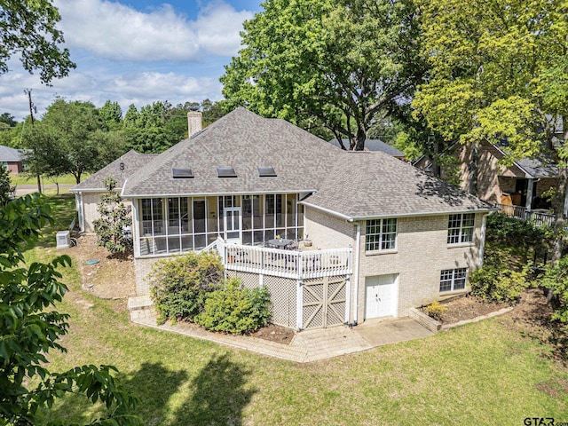 back of property featuring a chimney, brick siding, a lawn, a shingled roof, and a sunroom