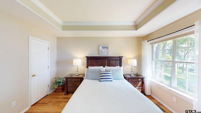 bedroom with baseboards, ornamental molding, a tray ceiling, and light wood-type flooring