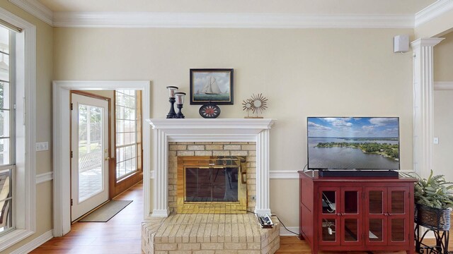 living area with wood finished floors, a brick fireplace, baseboards, and ornamental molding