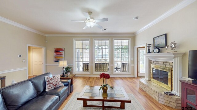 living room featuring a ceiling fan, a glass covered fireplace, crown molding, and light wood finished floors