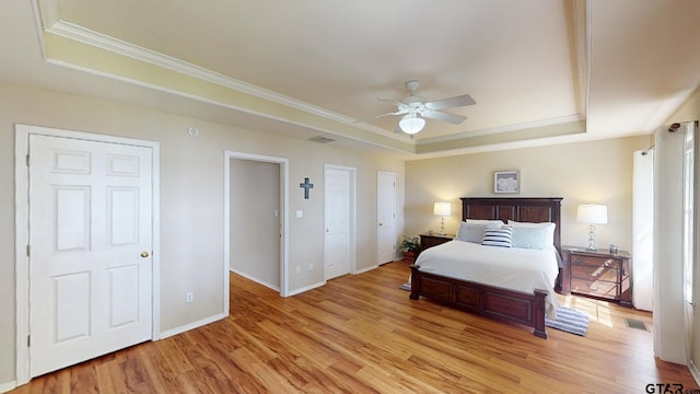 bedroom with crown molding, a tray ceiling, visible vents, and light wood-type flooring