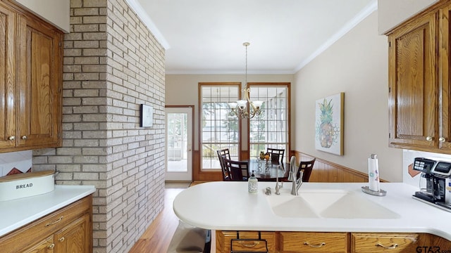 kitchen with brown cabinets, light countertops, wood finished floors, ornamental molding, and a chandelier
