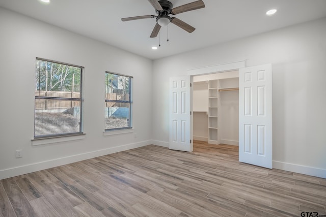 unfurnished bedroom featuring a spacious closet, a closet, ceiling fan, and light wood-type flooring