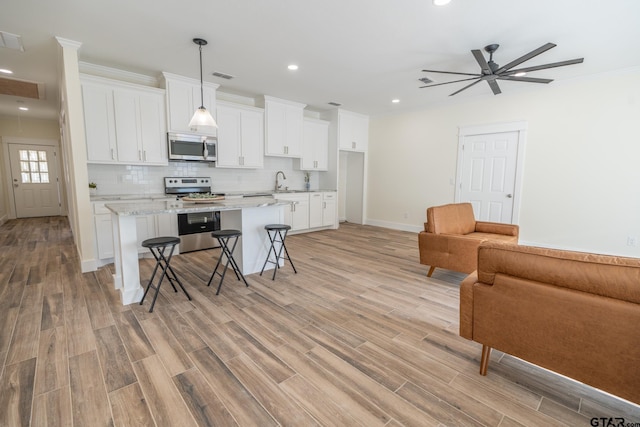 kitchen featuring a kitchen island, appliances with stainless steel finishes, a breakfast bar, white cabinets, and light stone countertops