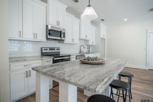 kitchen featuring a kitchen island, appliances with stainless steel finishes, a breakfast bar area, white cabinets, and light stone countertops