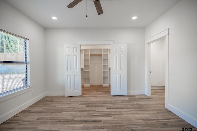 unfurnished bedroom with ceiling fan, a walk in closet, a closet, and light hardwood / wood-style flooring