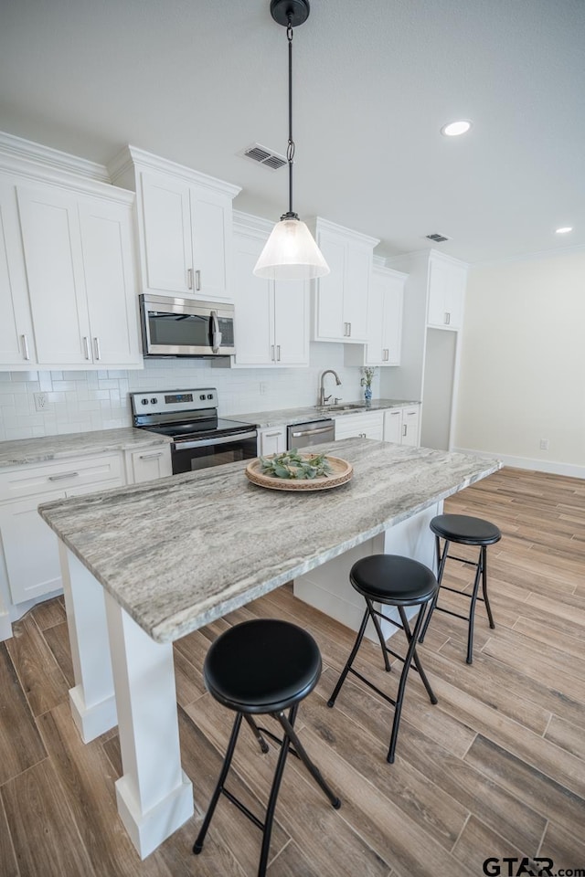 kitchen featuring pendant lighting, stainless steel appliances, white cabinets, and a kitchen island