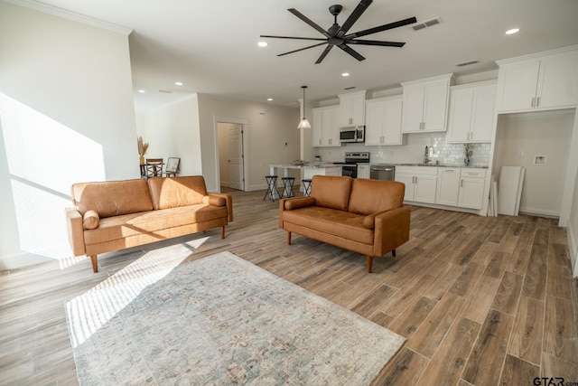 living room with sink, ornamental molding, light hardwood / wood-style floors, and ceiling fan