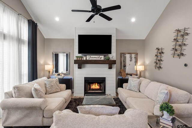 living room featuring ceiling fan, a large fireplace, and vaulted ceiling