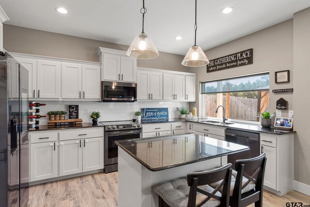 kitchen with sink, a kitchen island, backsplash, white cabinets, and appliances with stainless steel finishes