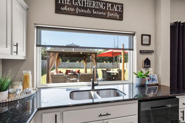 kitchen featuring dark stone countertops, sink, white cabinets, and stainless steel dishwasher