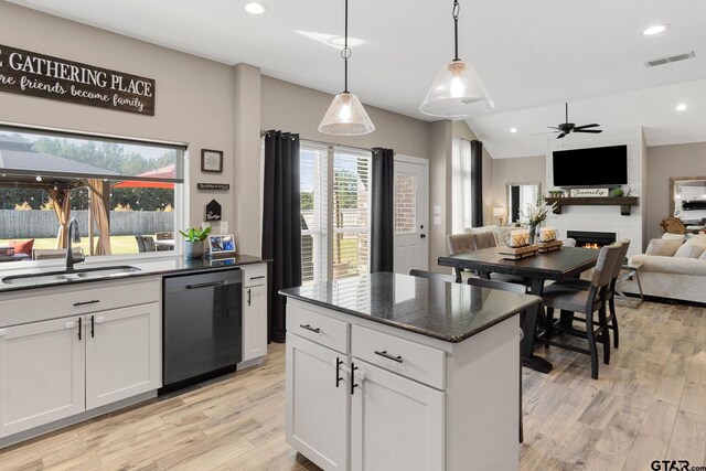 kitchen with sink, black dishwasher, pendant lighting, a fireplace, and white cabinets