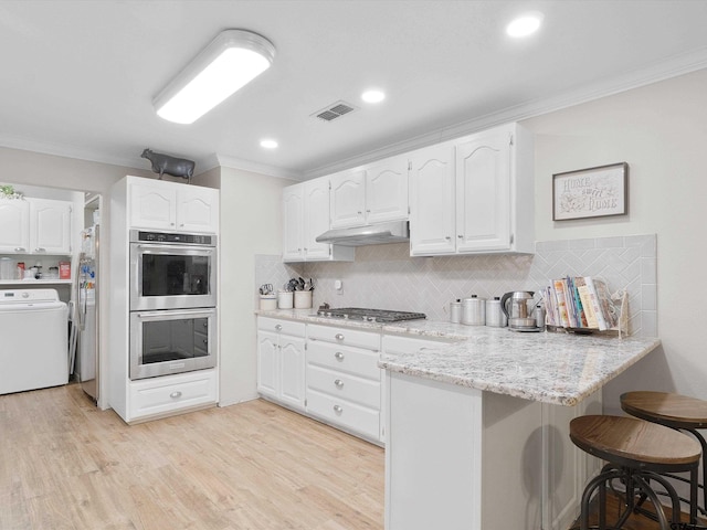 kitchen with tasteful backsplash, washer / dryer, a kitchen bar, white cabinets, and appliances with stainless steel finishes