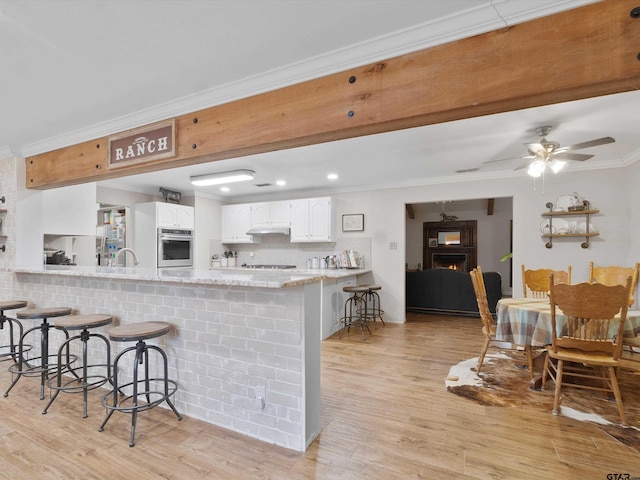 kitchen featuring a breakfast bar area, kitchen peninsula, white cabinetry, and oven