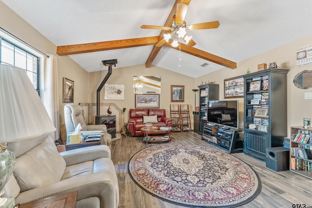 living room featuring a textured ceiling, light hardwood / wood-style floors, lofted ceiling with beams, and a wood stove