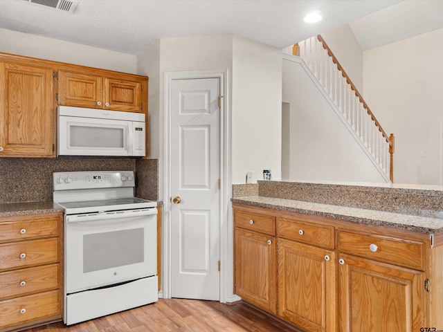 221 Butternut Gln, Holly Lake Ranch, TX 75765 - kitchen with white appliances, light wood finished floors, brown cabinets, light stone counters, and tasteful backsplash