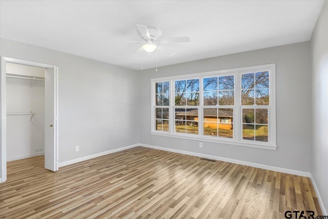 unfurnished bedroom with a walk in closet, a closet, ceiling fan, and light wood-type flooring