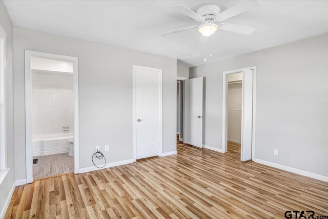 unfurnished bedroom featuring ensuite bath, a spacious closet, a closet, and light hardwood / wood-style flooring