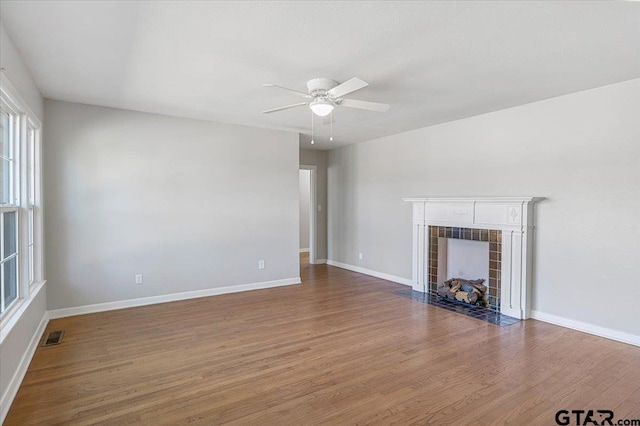 unfurnished living room featuring a tiled fireplace, wood-type flooring, and ceiling fan