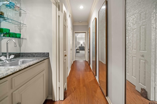 corridor with baseboards, crown molding, a sink, and light wood-style floors