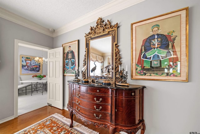hallway with wood finished floors, a textured ceiling, ornamental molding, and an inviting chandelier