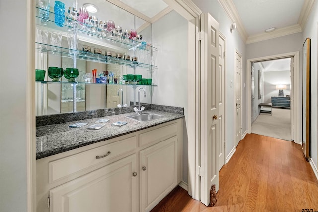 bar with indoor wet bar, ornamental molding, a sink, and light wood-style flooring