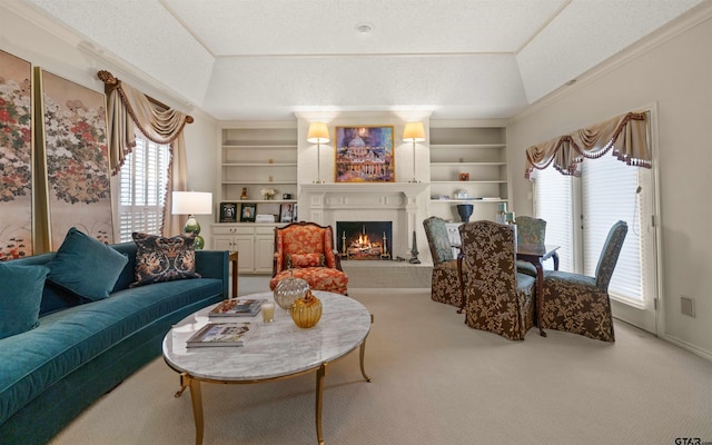 living room with a warm lit fireplace, carpet floors, built in features, and a raised ceiling