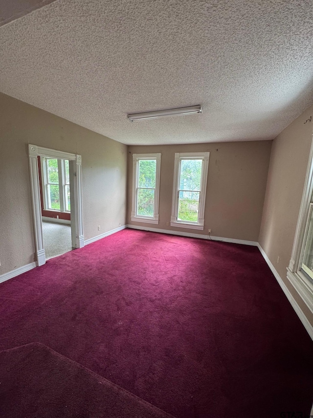 carpeted spare room featuring a textured ceiling, plenty of natural light, and baseboards