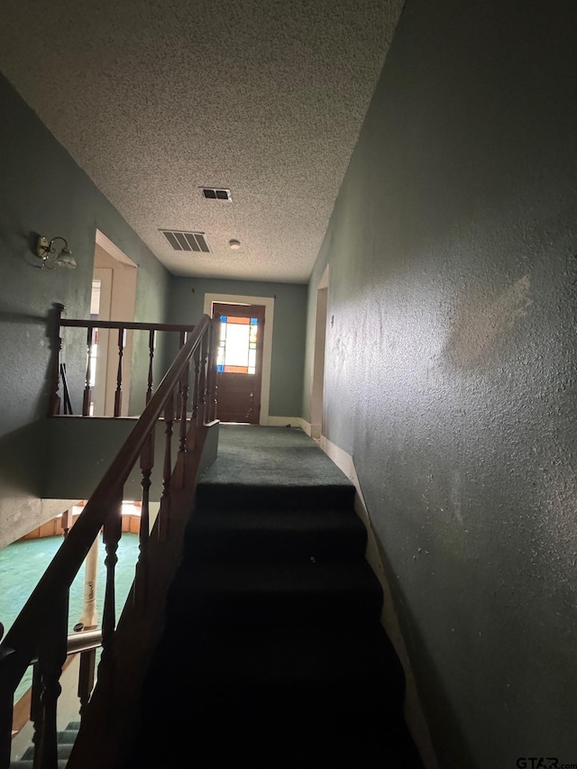 staircase with carpet floors, a textured ceiling, visible vents, and baseboards