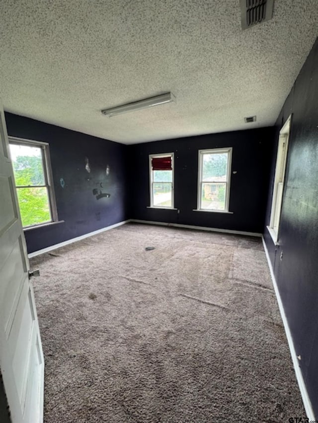carpeted empty room featuring a textured ceiling, visible vents, and baseboards
