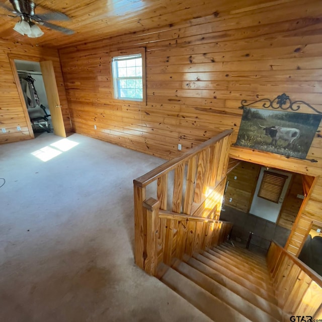 staircase featuring wood walls, ceiling fan, and wooden ceiling