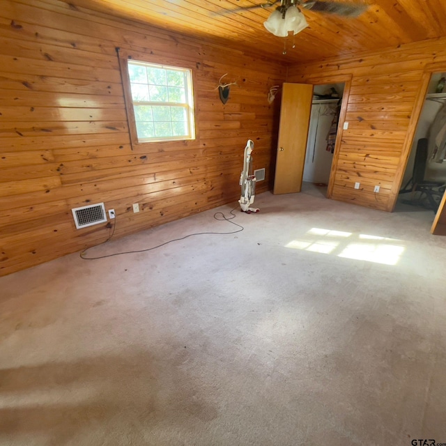 carpeted spare room featuring ceiling fan, wood walls, and wooden ceiling