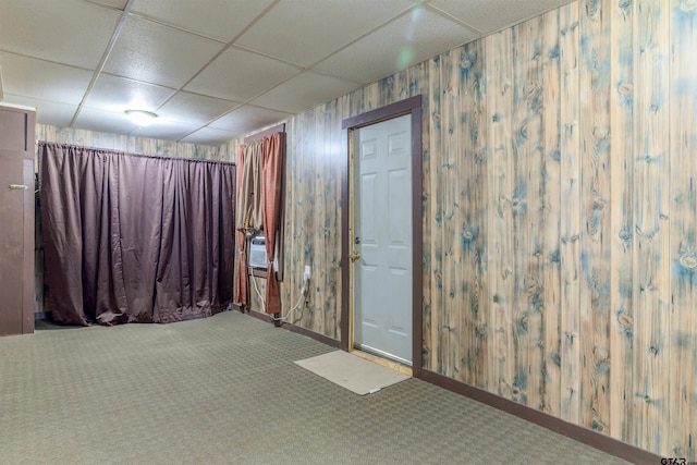 empty room featuring carpet flooring, a drop ceiling, and wood walls