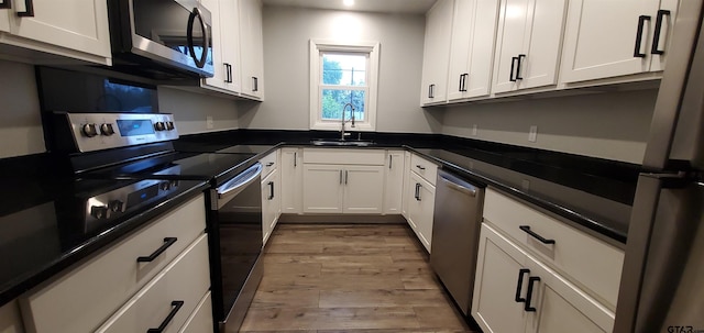 kitchen with a sink, light wood-style floors, white cabinets, appliances with stainless steel finishes, and dark countertops