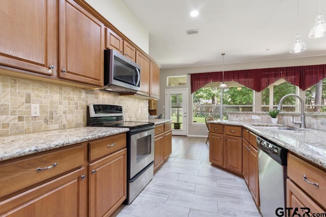 9190 Teal Flight Way, Tyler, TX 75703 - kitchen featuring appliances with stainless steel finishes, a sink, brown cabinetry, and light stone countertops