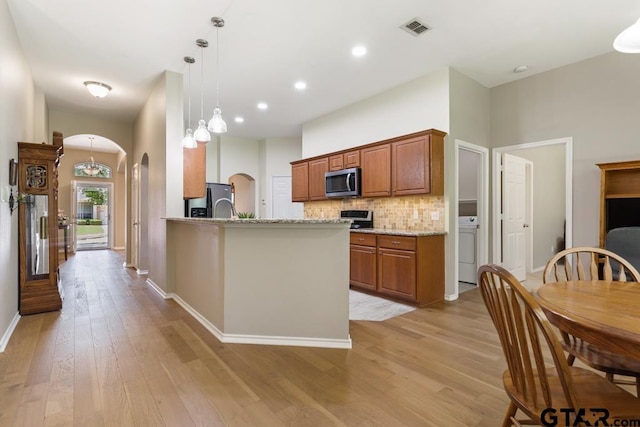 9190 Teal Flight Way, Tyler, TX 75703 - kitchen with appliances with stainless steel finishes, arched walkways, light wood-style floors, brown cabinets, and decorative backsplash