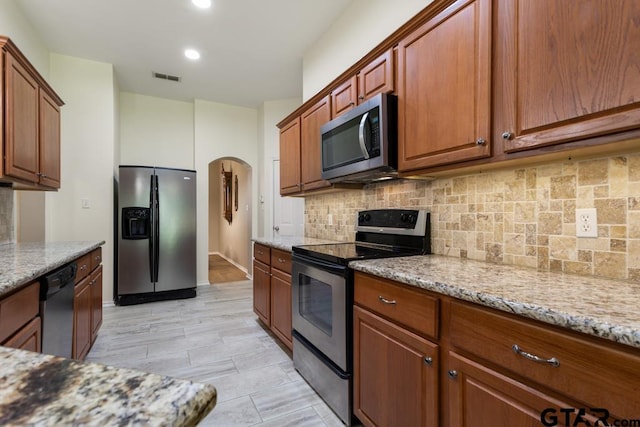 9190 Teal Flight Way, Tyler, TX 75703 - kitchen with stainless steel appliances, arched walkways, light stone counters, backsplash, and brown cabinetry