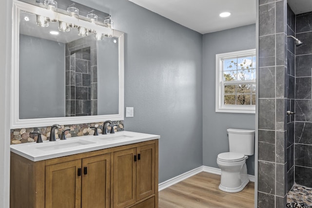 bathroom with a tile shower, hardwood / wood-style floors, vanity, and toilet