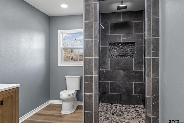 bathroom with wood-type flooring, a tile shower, vanity, and toilet