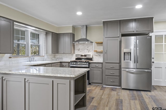 kitchen with gray cabinetry, stainless steel appliances, kitchen peninsula, and wall chimney range hood