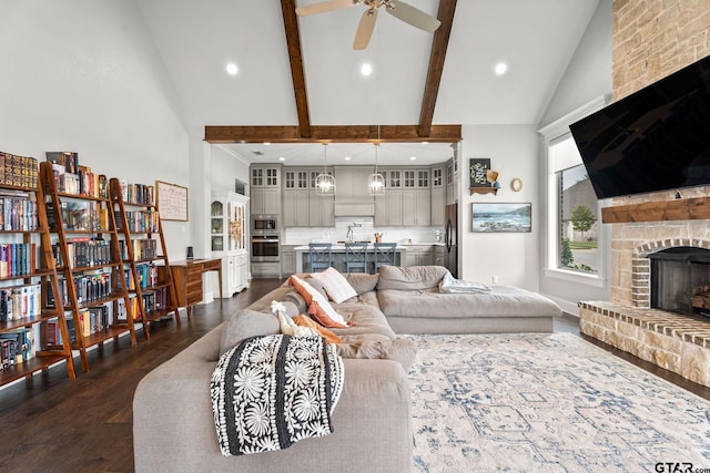 living room with a fireplace, high vaulted ceiling, beam ceiling, dark wood-type flooring, and ceiling fan