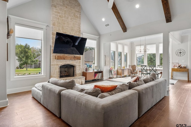 living room with wood-type flooring, beam ceiling, a stone fireplace, high vaulted ceiling, and a notable chandelier