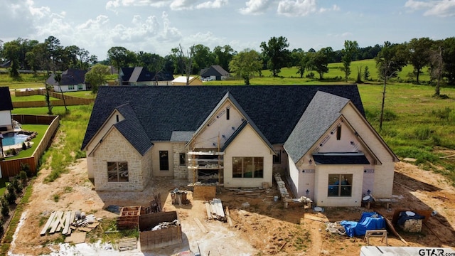 view of front of home featuring stone siding, roof with shingles, and fence