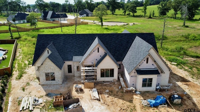 view of front facade featuring stone siding, a shingled roof, and fence