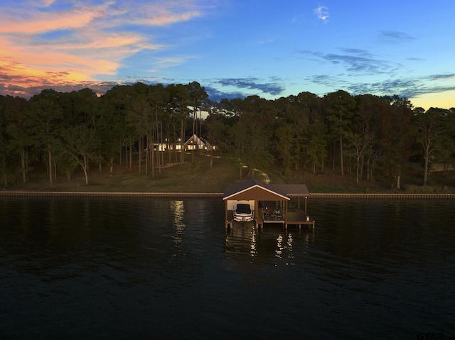 view of dock with a water view, boat lift, and a wooded view