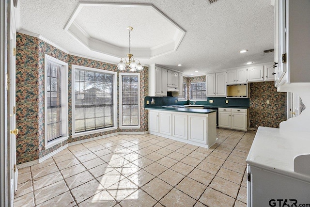 kitchen with an inviting chandelier, a raised ceiling, pendant lighting, a textured ceiling, and white cabinets