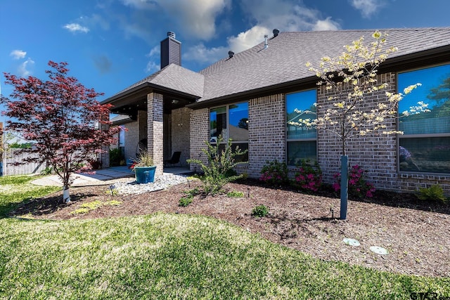 7317 Hearthstone Ln, Tyler, TX 75703 - back of house featuring brick siding, a chimney, a shingled roof, and a lawn
