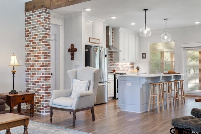 15988 C R 1151, Tyler, TX 75704 - kitchen featuring appliances with stainless steel finishes, wall chimney range hood, light wood finished floors, a breakfast bar area, and white cabinets