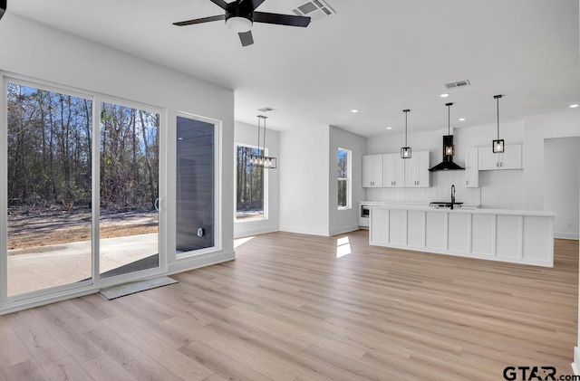 unfurnished living room with sink, ceiling fan with notable chandelier, and light wood-type flooring