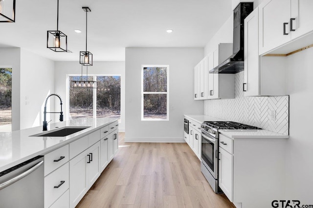 kitchen with appliances with stainless steel finishes, decorative light fixtures, sink, white cabinets, and wall chimney exhaust hood